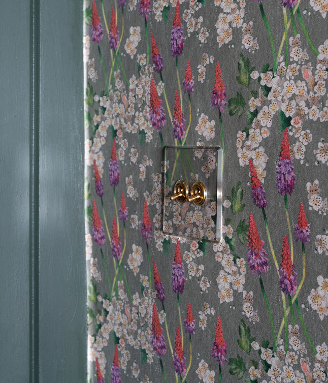 A close-up of a textured floral wallpaper featuring vibrant red and purple flowers, with a clear light switch embedded.