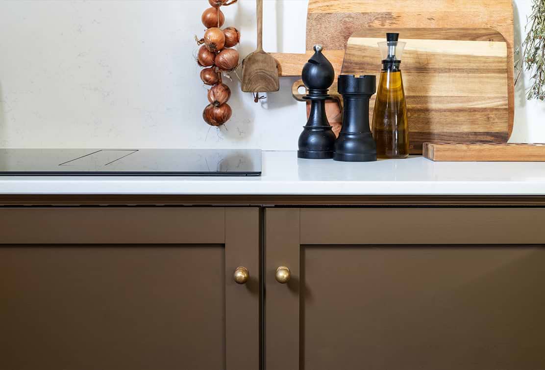 A stylish kitchen countertop featuring a black cooktop, wooden cutting boards, spice containers, a wooden spoon, and hanging onions.