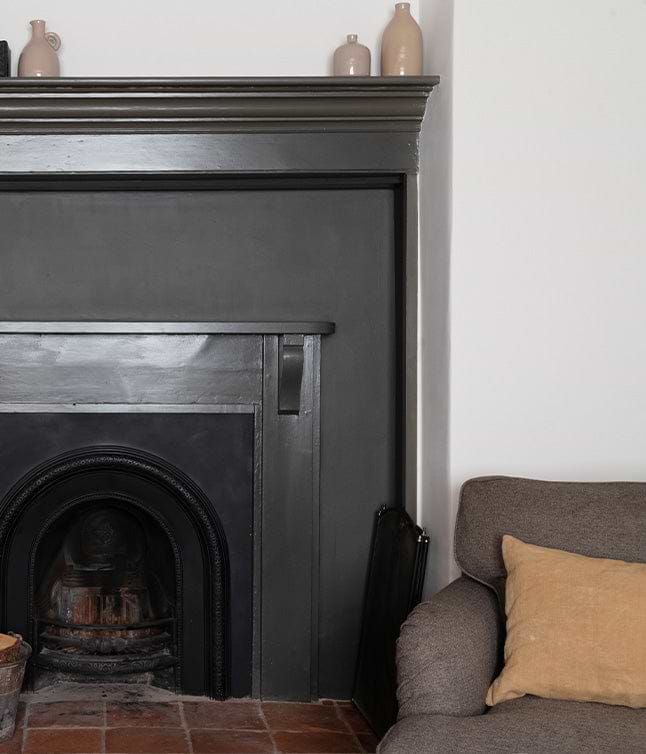 A rustic living space featuring a dark fireplace, beige couch with a throw pillow, and decorative candles on the mantel.