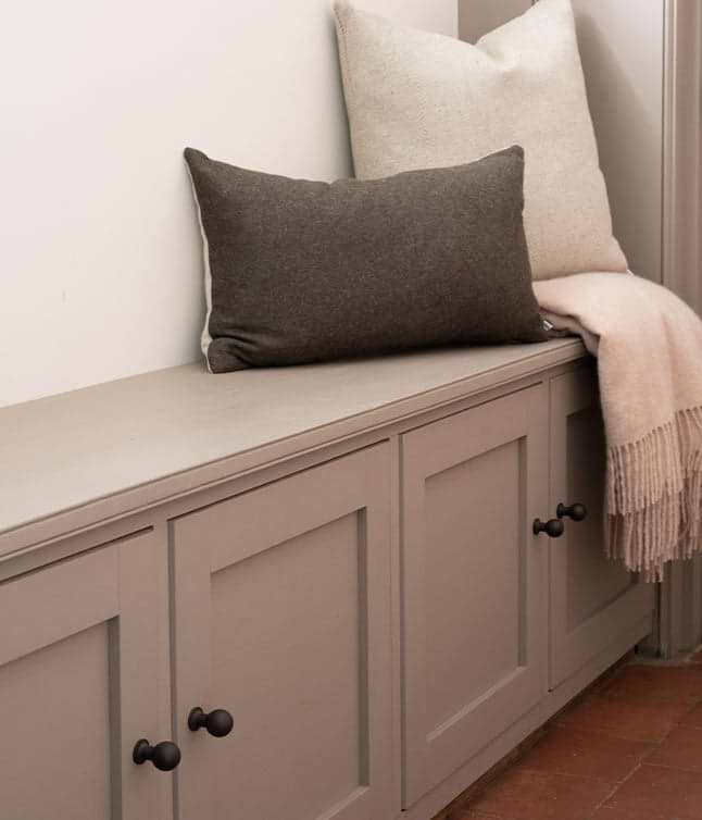 Cozy seating area featuring a gray bench with bronze knobs, adorned with plush pillows and a soft throw blanket.