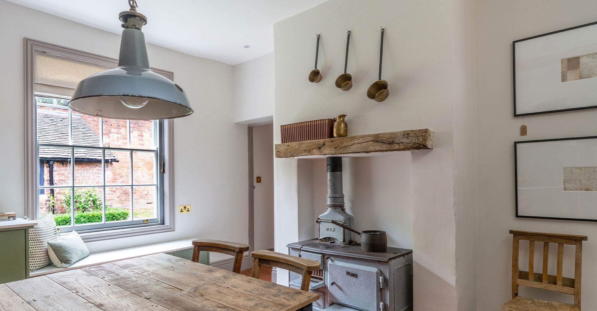 Cozy kitchen interior featuring a wooden table, vintage stove, and decorative items on a rustic shelf, illuminated by a pendant light.