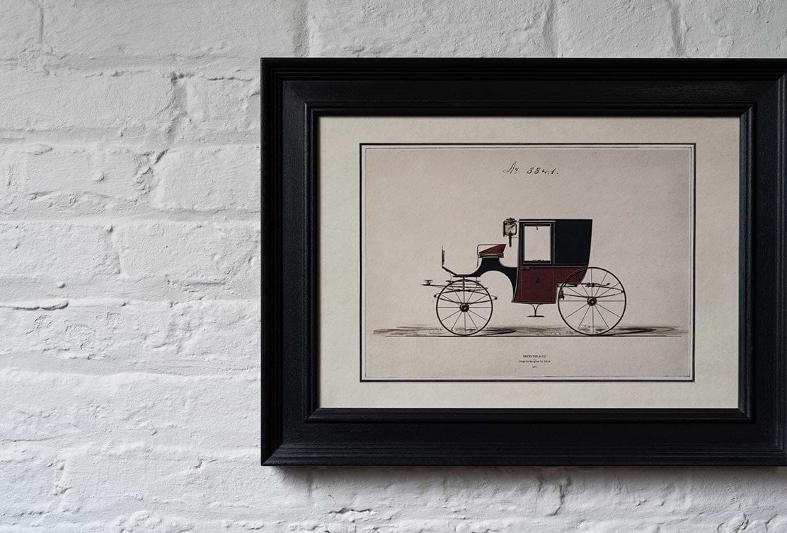 Framed vintage illustration of a horse-drawn carriage in maroon and black, displayed against a textured white brick wall.