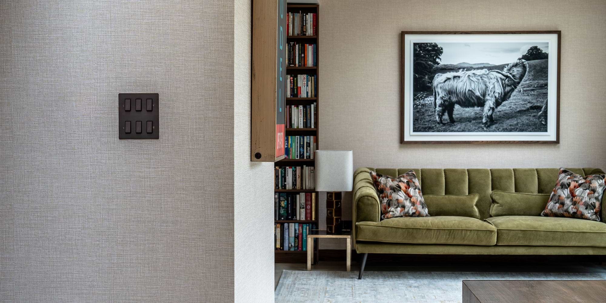 A cozy living room featuring a green velvet sofa with patterned pillows, a bookshelf, and a black-and-white cow photograph on the wall.