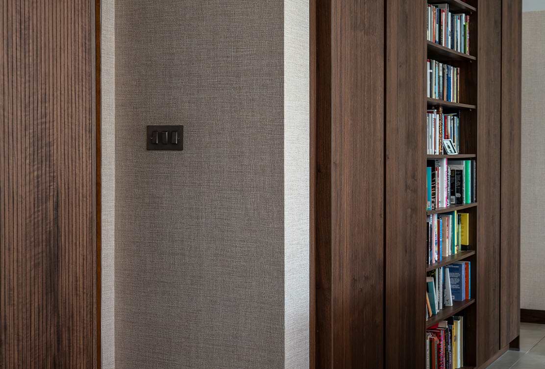 A close-up of a textured wall featuring a light switch, adjacent to a wooden bookshelf filled with colorful books.