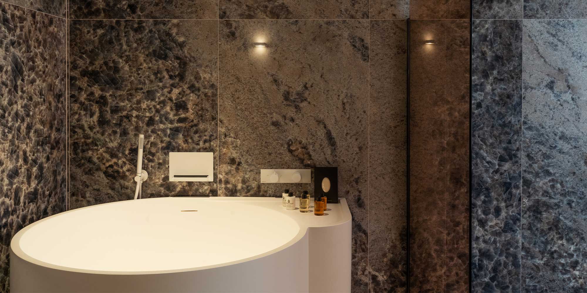 A stylish modern bathroom featuring a round white bathtub against textured stone walls, adorned with elegant toiletries.
