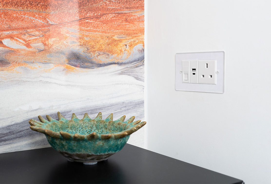 A textured turquoise ceramic bowl sits on a black surface, against a vibrant, marbled orange and grey wall, next to a white power outlet.