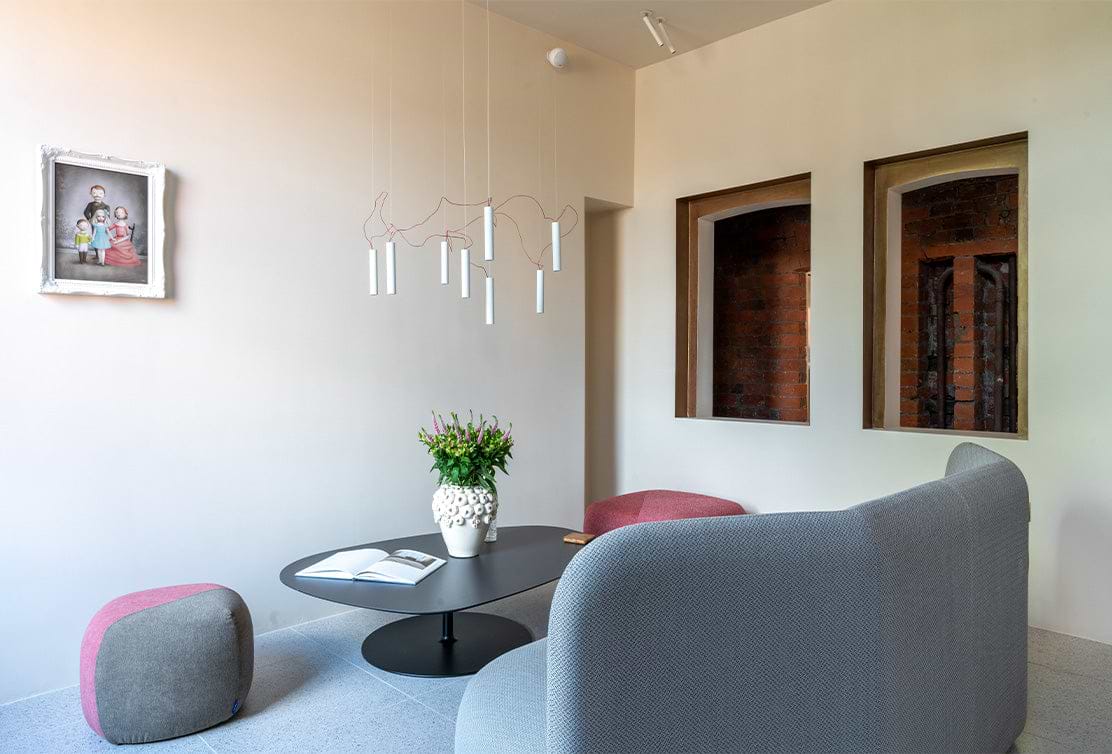 A modern living space featuring a round table with a vase of flowers, cozy seating, artistic lighting, and a framed portrait on the wall.