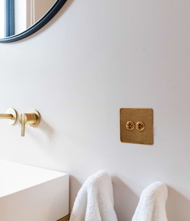A minimalist bathroom corner featuring a round mirror, gold fixtures, and a white counter with hanging towels.