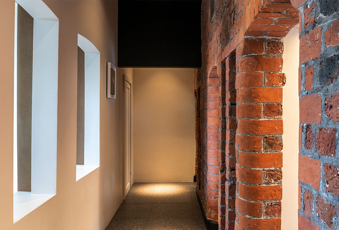 A modern hallway featuring exposed brick columns, light-colored walls, and subtle lighting creating a warm, inviting atmosphere.