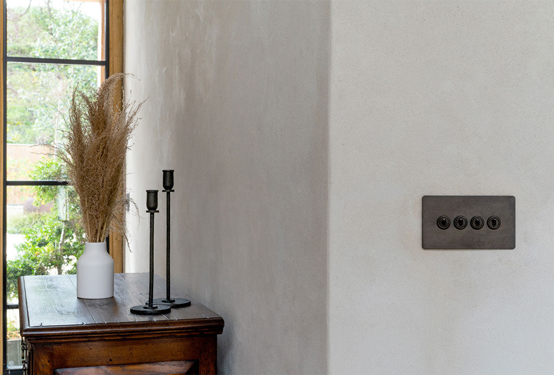 A minimalist interior featuring a textured wall, a wooden table with a white vase of pampas grass, and black candle holders.