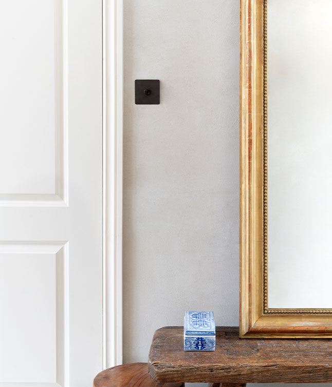 A wooden table holds a decorative blue and white box next to a large golden-framed mirror, against a light gray wall.