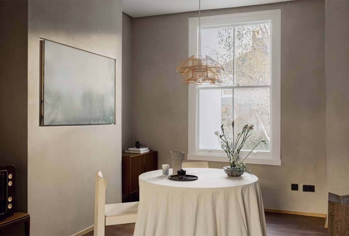 Cozy dining area featuring a round table with a white tablecloth, flower arrangement, pendant light, and minimalistic decor.