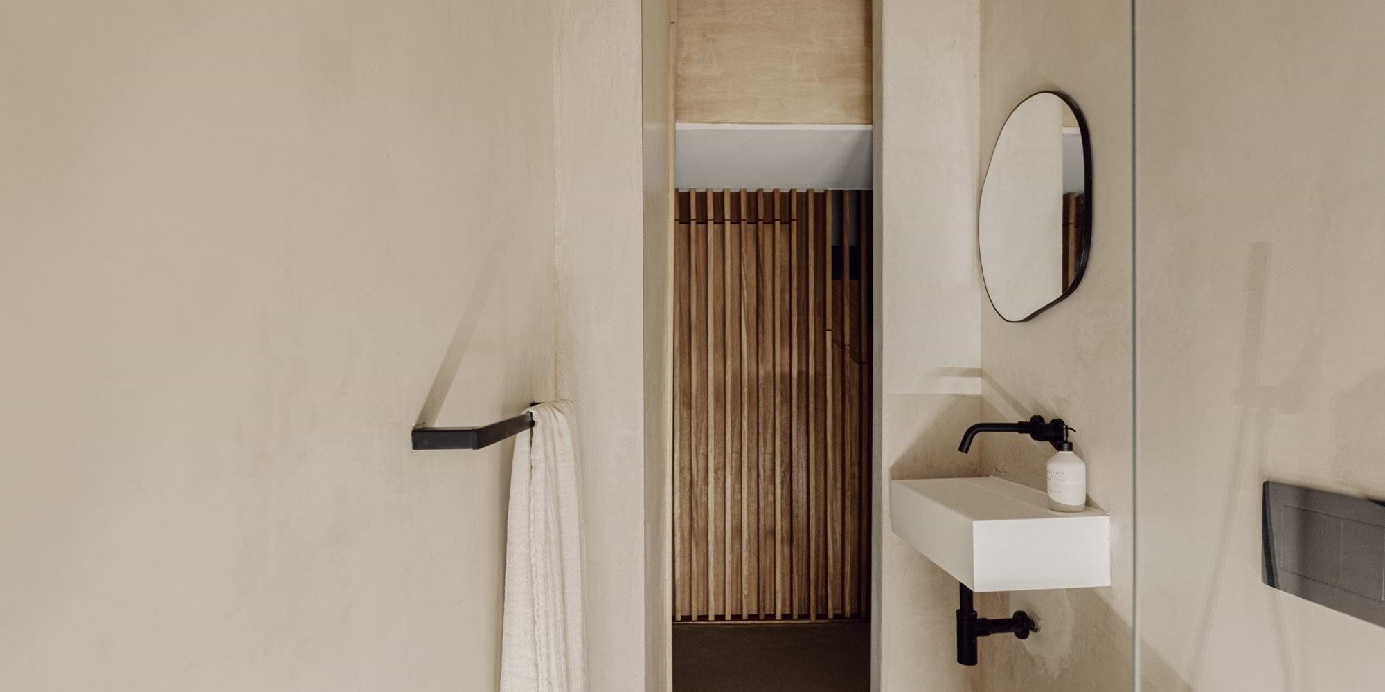 A modern bathroom featuring a white sink, black faucet, round mirror, and a towel on a rack, with wooden paneling in the background. 