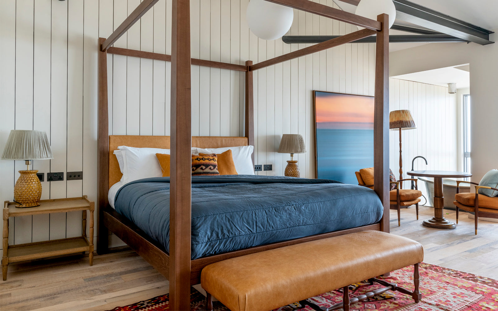 A stylish bedroom featuring a four-poster bed, cozy decor, and a calming beach landscape painting for inspiration.