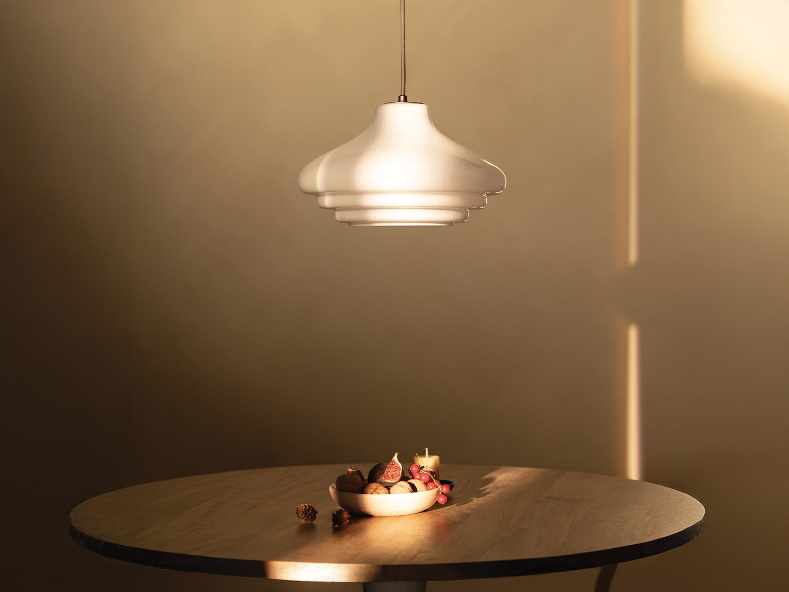A stylish white pendant lamp hangs above a wooden table adorned with a bowl of decorative items and a small candle. Soft light glows.