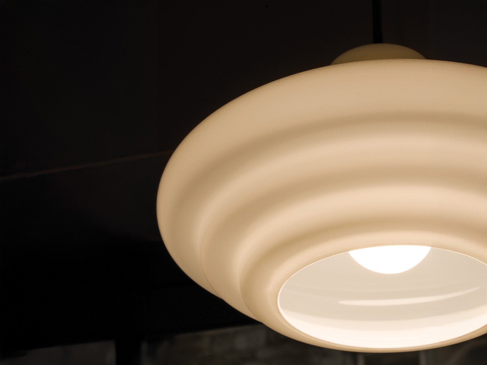 A close-up view of a round, cream-colored pendant light with subtle ribbed texture and a soft white bulb glowing inside.