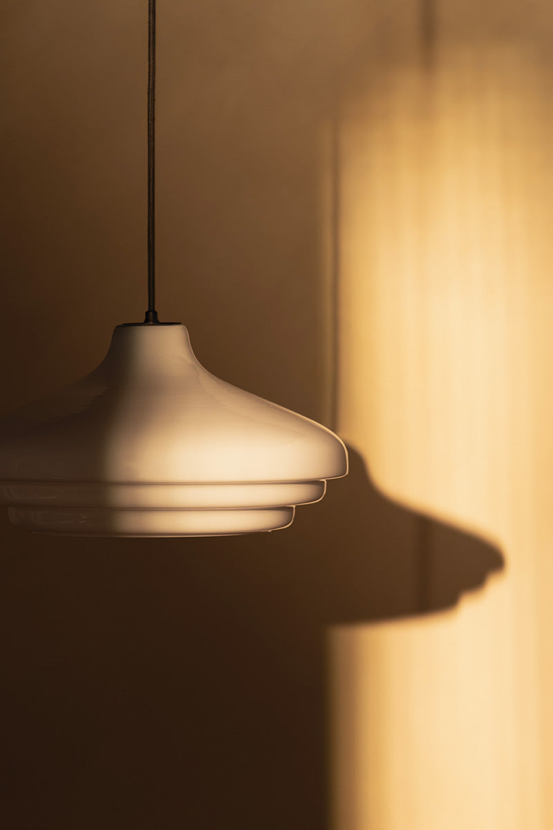 A modern pendant light casts a soft shadow on a textured wall, illuminated by warm, natural sunlight.