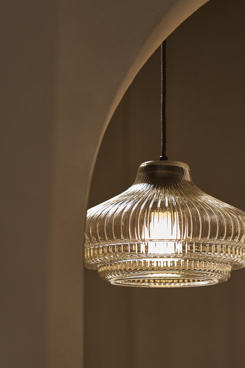 A close-up of a stylish, ribbed glass pendant lamp casting a warm glow against a neutral backdrop.