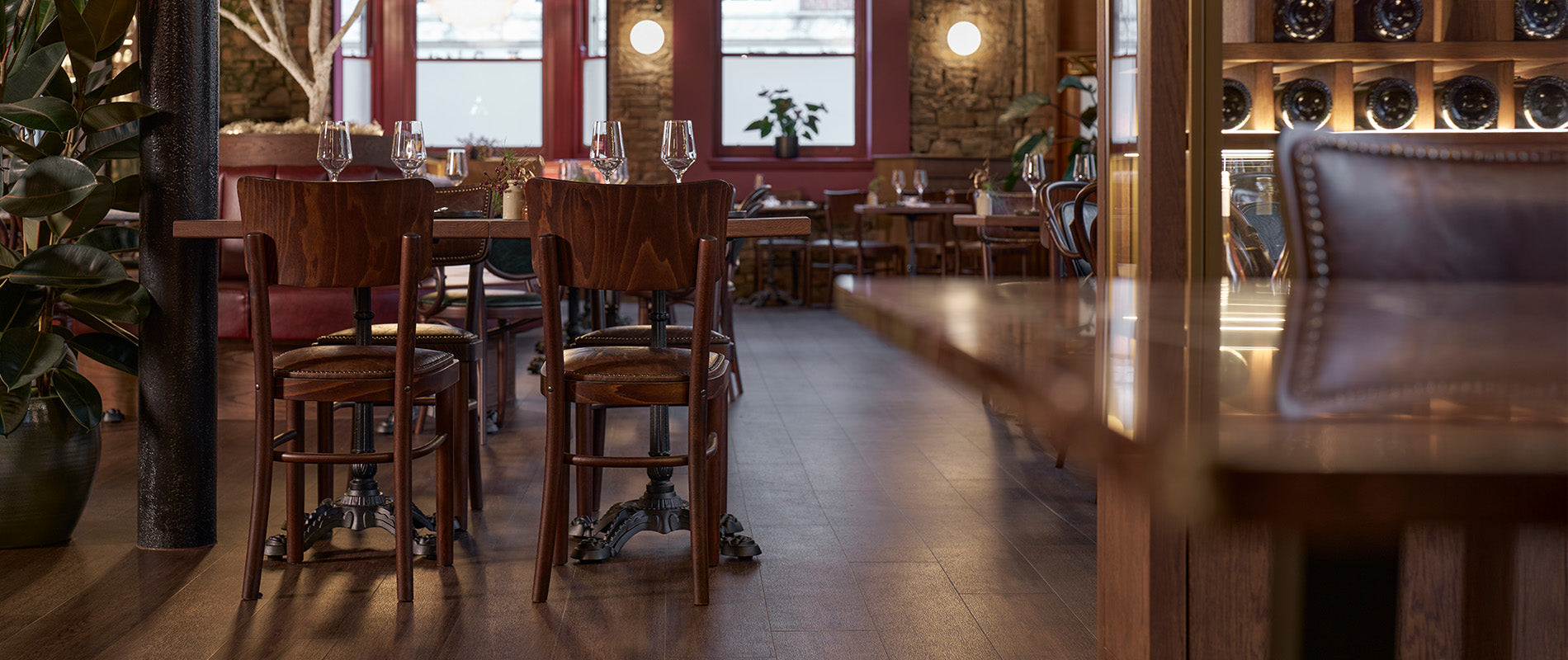 A cosy restaurant interior featuring wooden tables and chairs, dim lighting, and lush greenery, creating an inviting atmosphere.