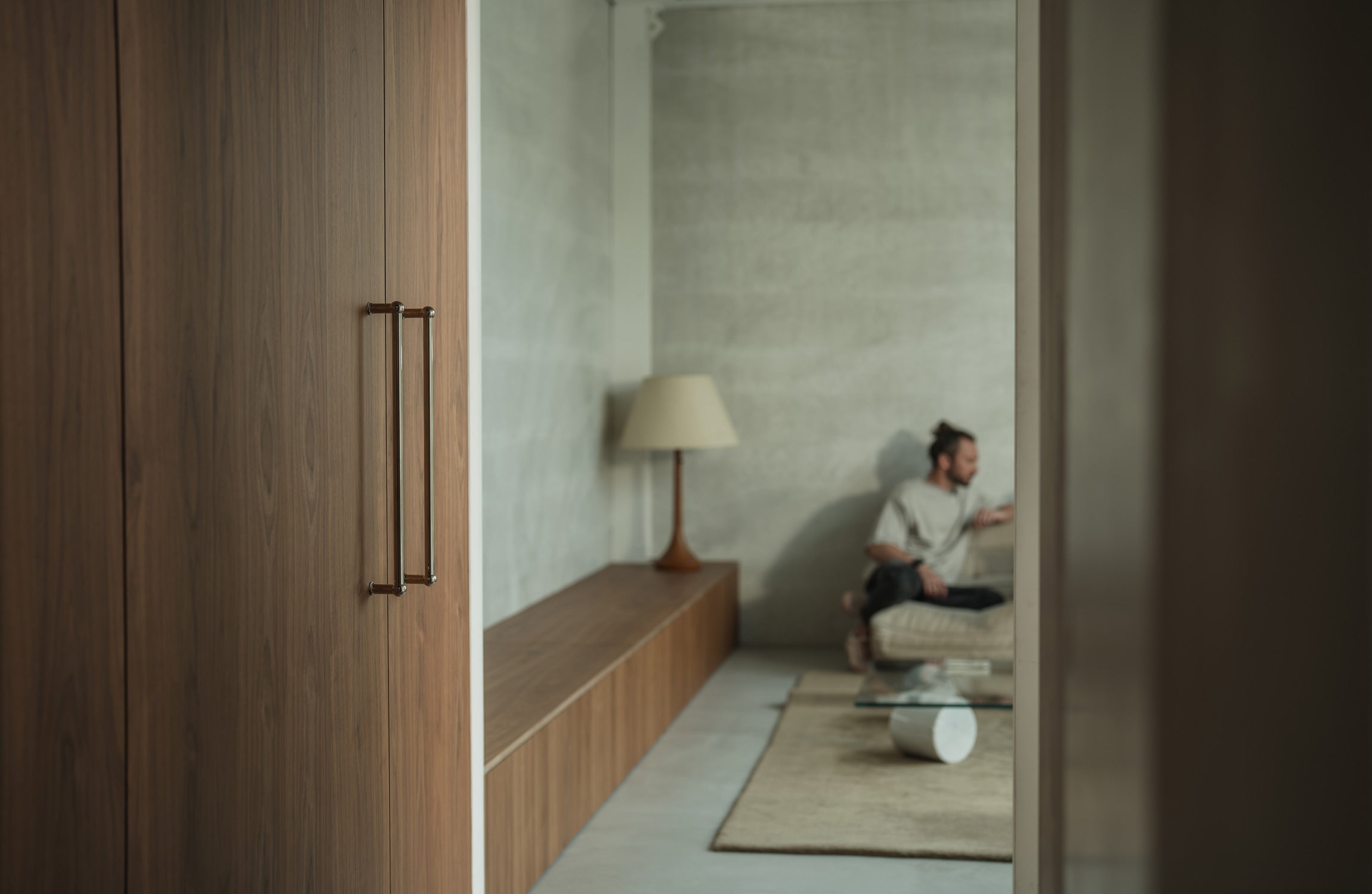 A cozy living space featuring a wooden wardrobe, beige sofa, round coffee table, and a floor lamp against a textured wall.