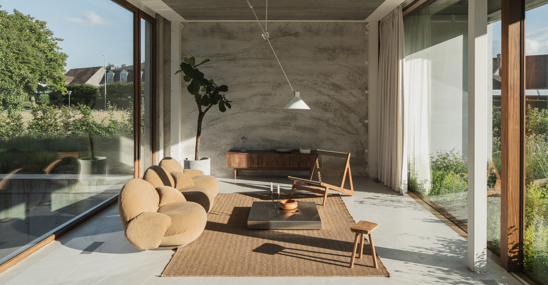 A modern, sunlit living room features curved beige sofas, a wooden coffee table, and a potted plant, creating a cozy atmosphere.