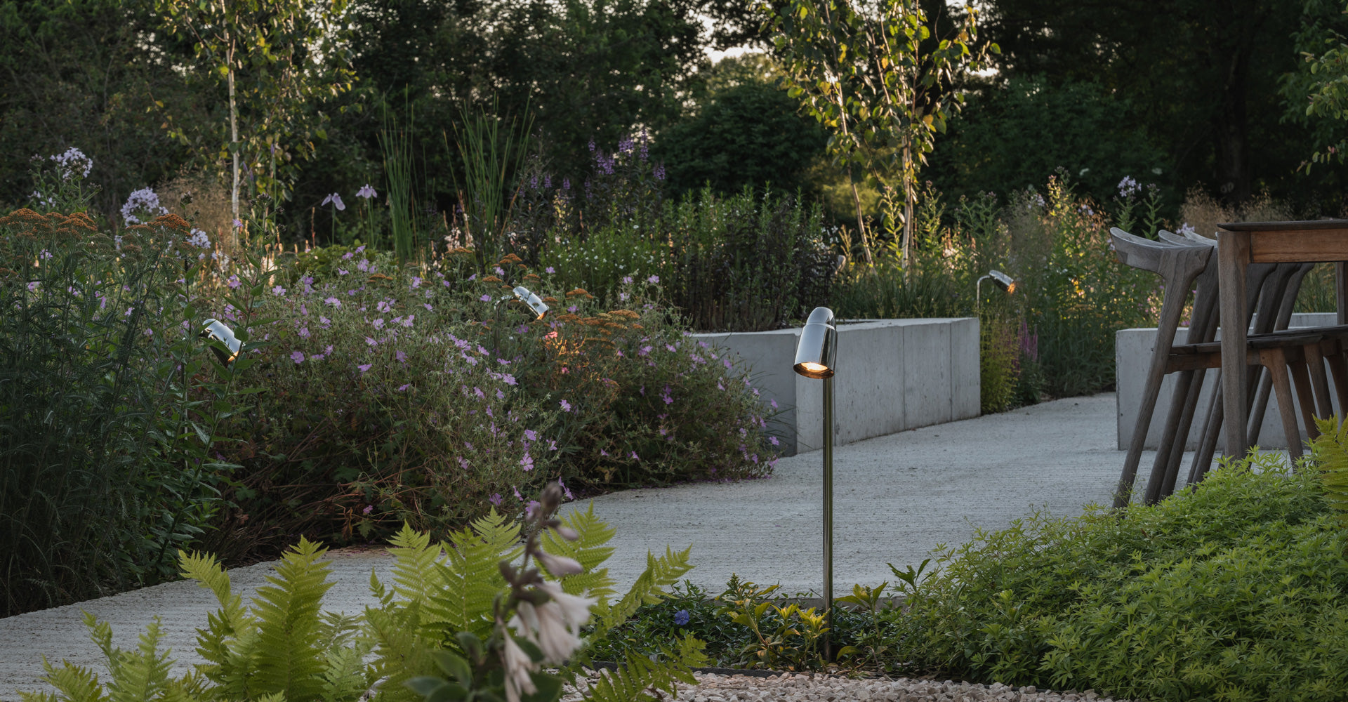 A tranquil garden pathway lined with blooming flowers and modern, sleek outdoor lights illuminating the scene at dusk.