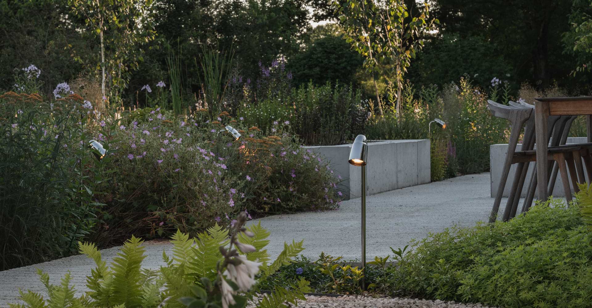 A tranquil garden pathway lined with blooming flowers and modern, sleek outdoor lights illuminating the scene at dusk.