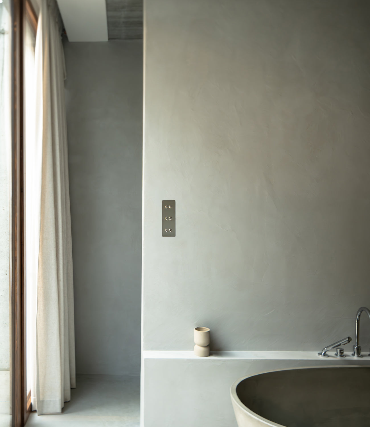 Minimalist bathroom featuring a smooth gray wall, a modern light switch, a soft curtain, and a minimalist vessel on a ledge.