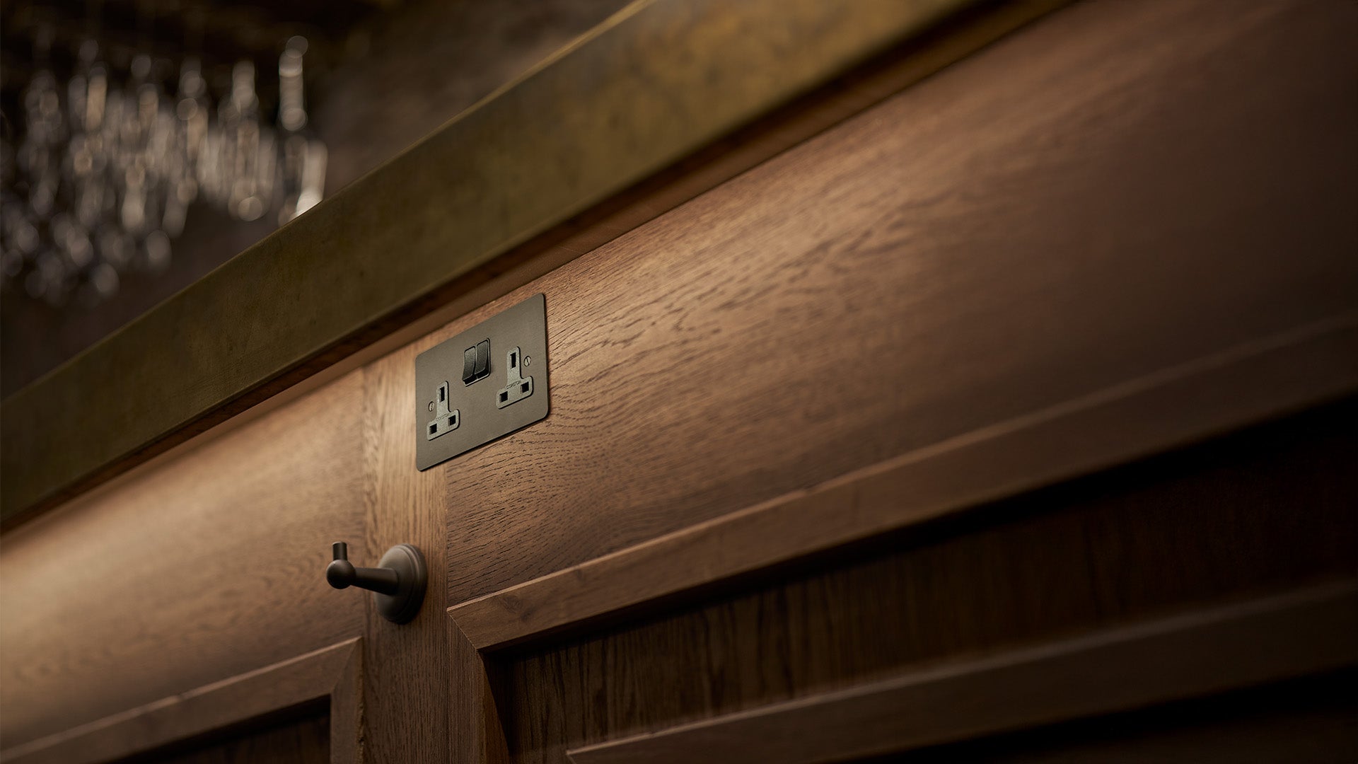 Close-up of a wooden cabinet surface featuring a black electrical socket and a metal knob against a blurred backdrop.