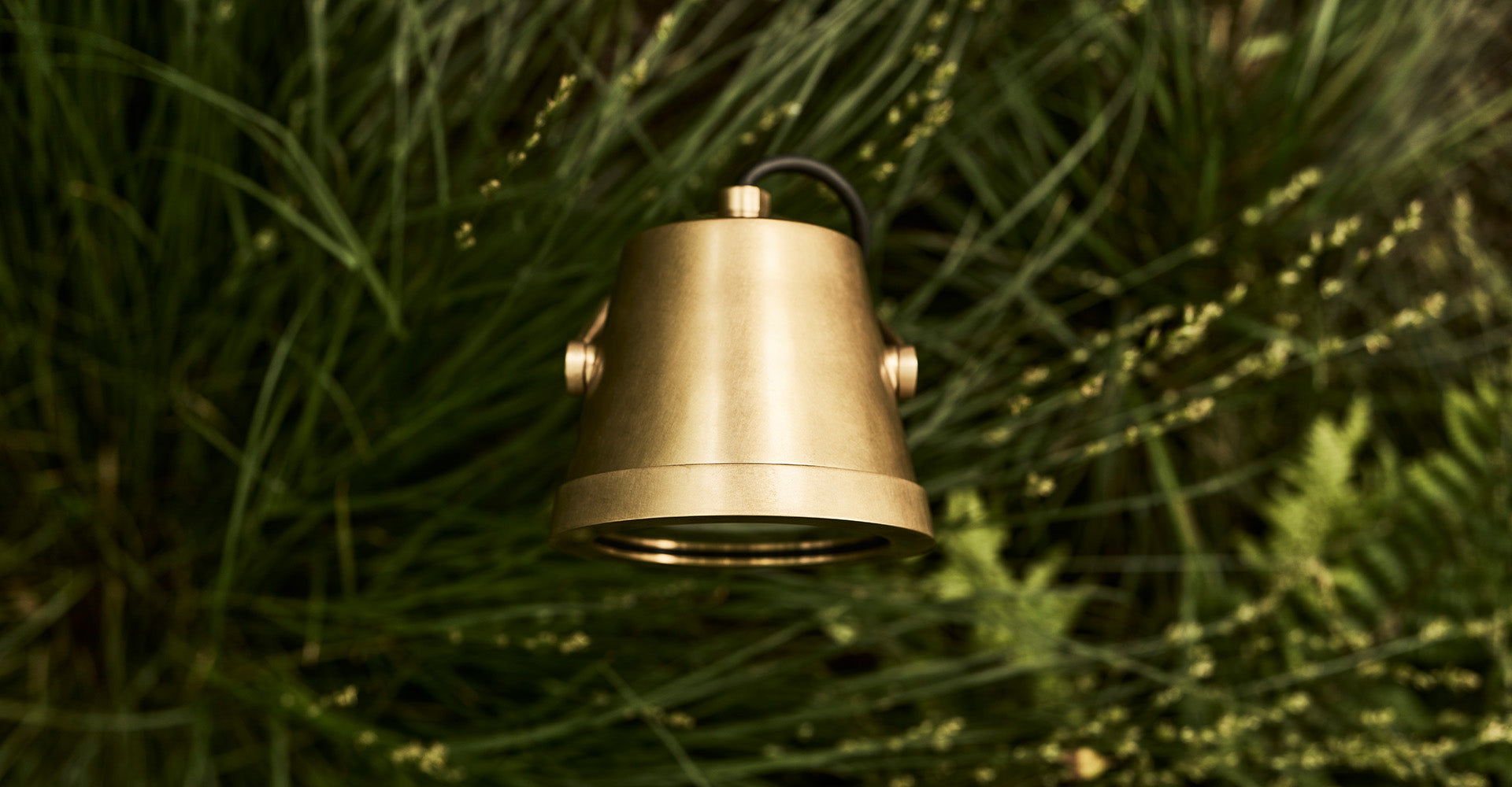 A birds-eye view of a sleek brass floodlight within lush green grass, blending modern design with natural elements.