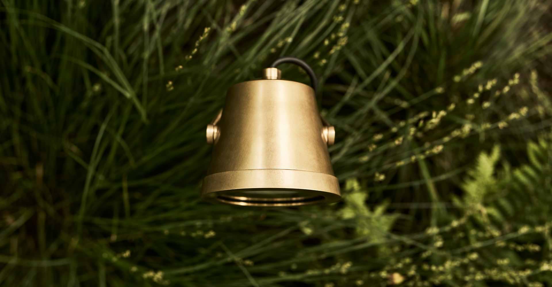 A birds-eye view of a sleek brass floodlight within lush green grass, blending modern design with natural elements.