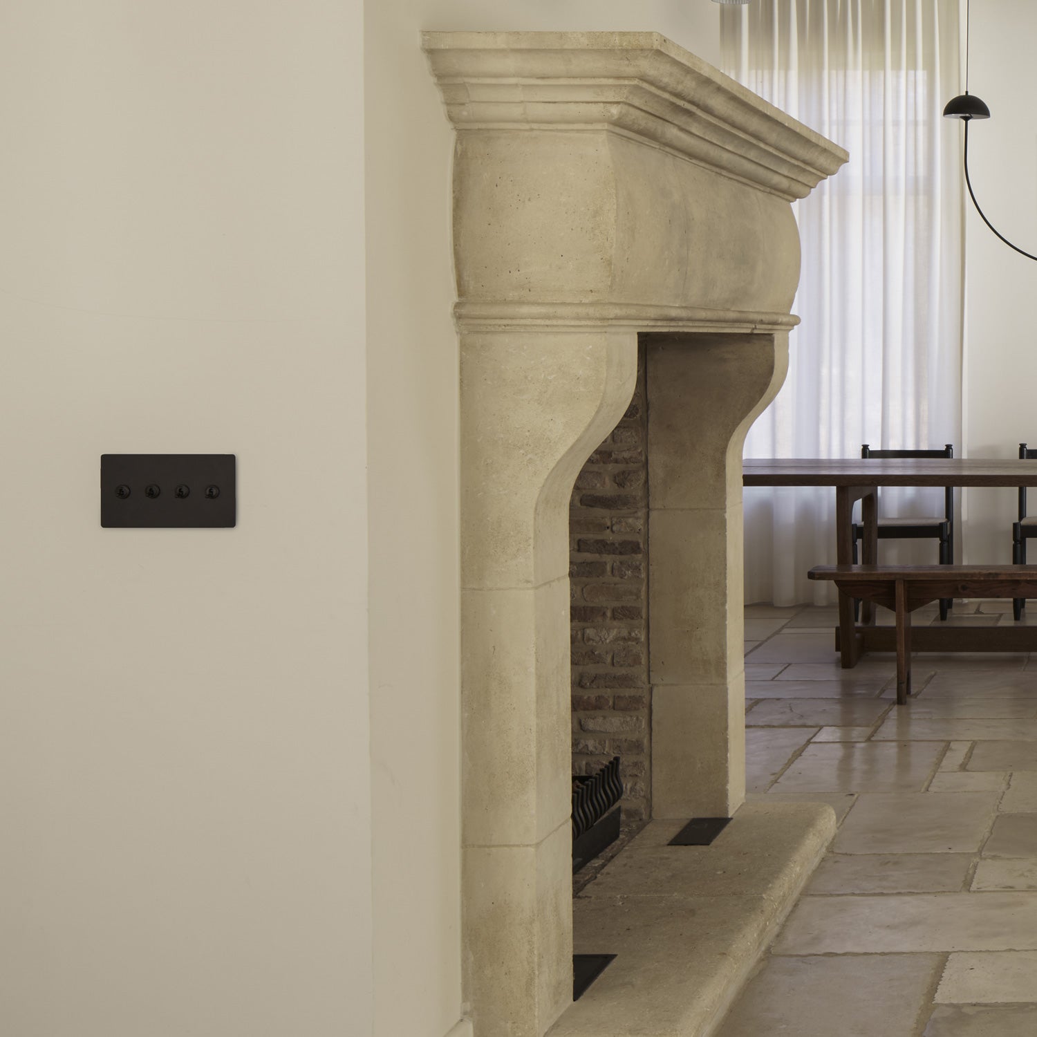 A modern living space featuring a stone fireplace, elegant wall sconces, and a minimalist dining area with a simple table and chairs.