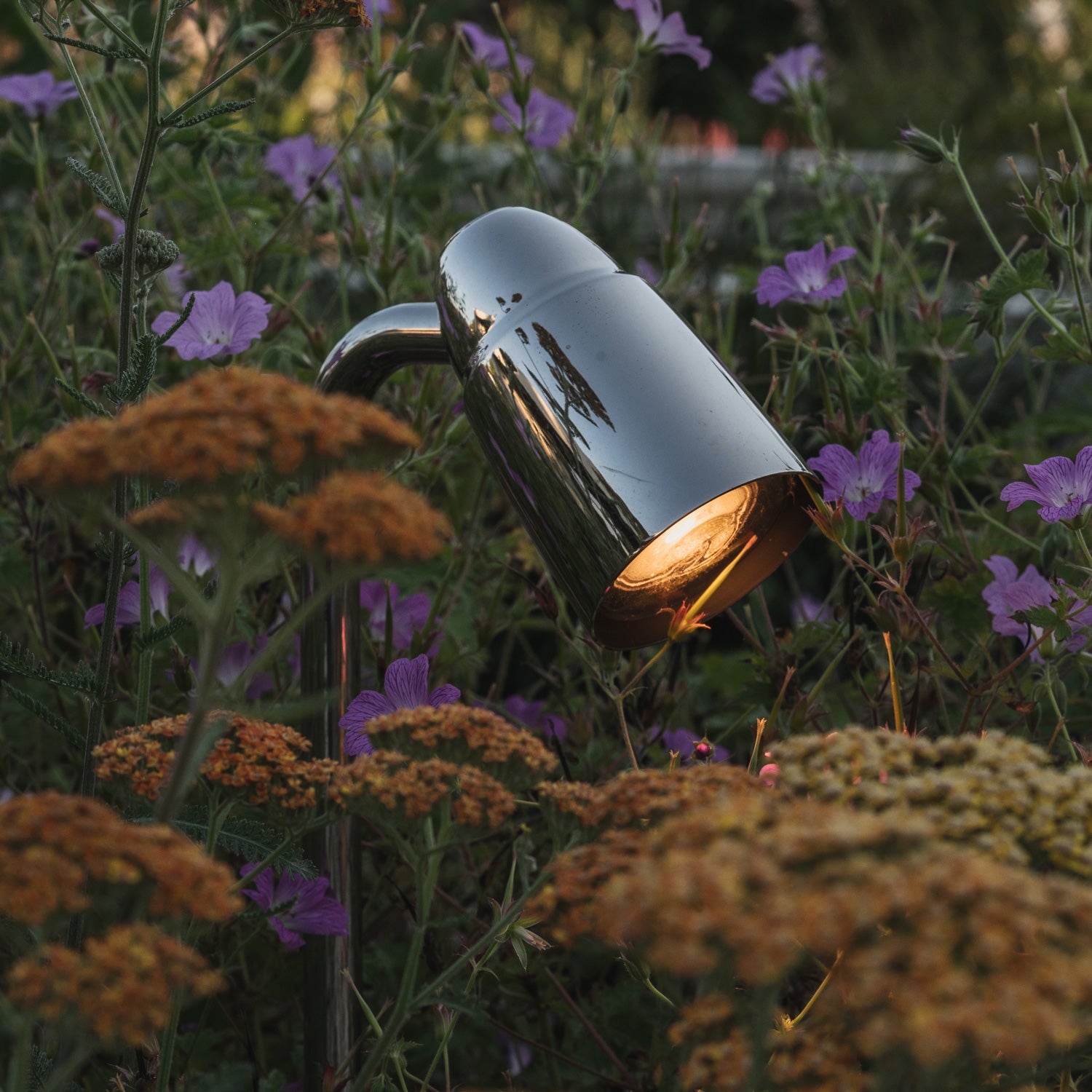 A sleek garden lamp emits warm light amidst vibrant flowers, enhancing the serene outdoor atmosphere.