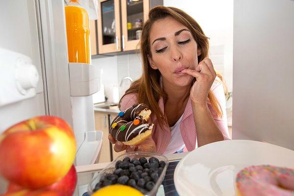 Woman suffering from stress and hormonal imbalance because of her high-sugar diet, as she's eating a donut