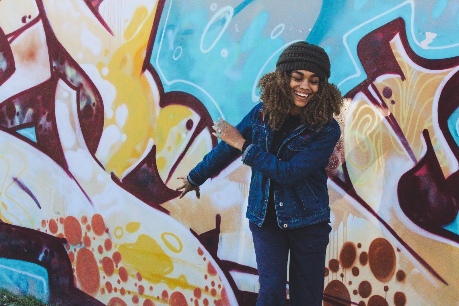 A happy woman in front of a colorful wall of graffiti