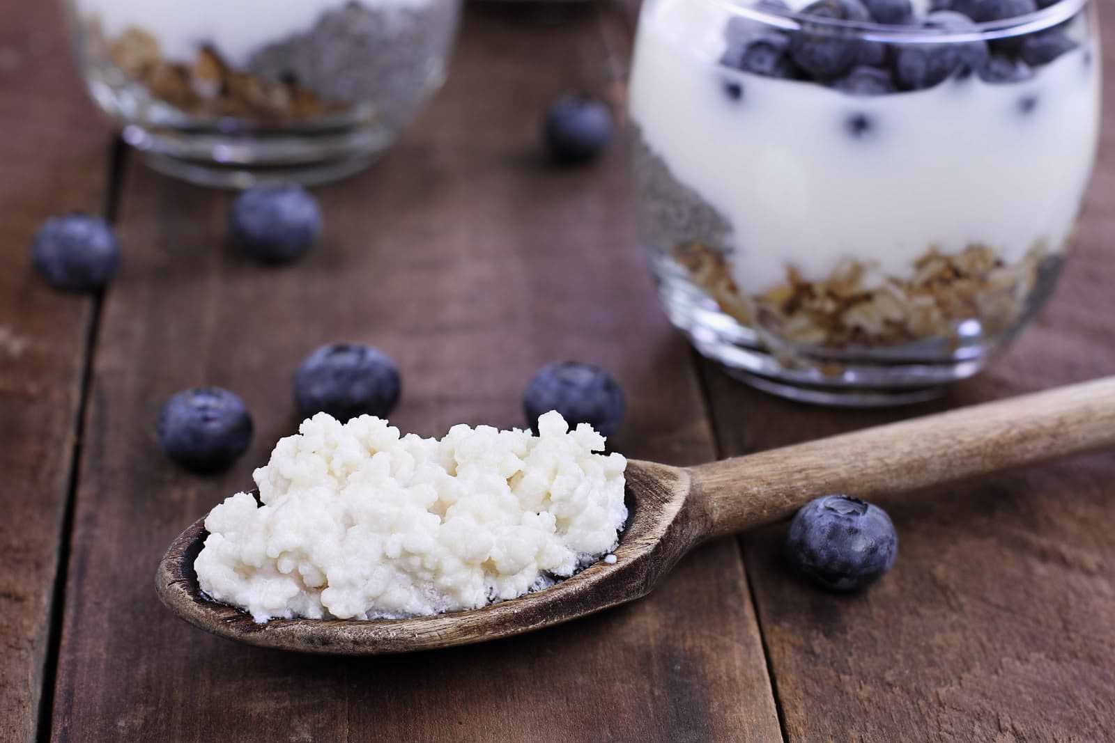 Kefir vs. yogurt: kefir grain on a spoon in front of cups of blueberry kefir