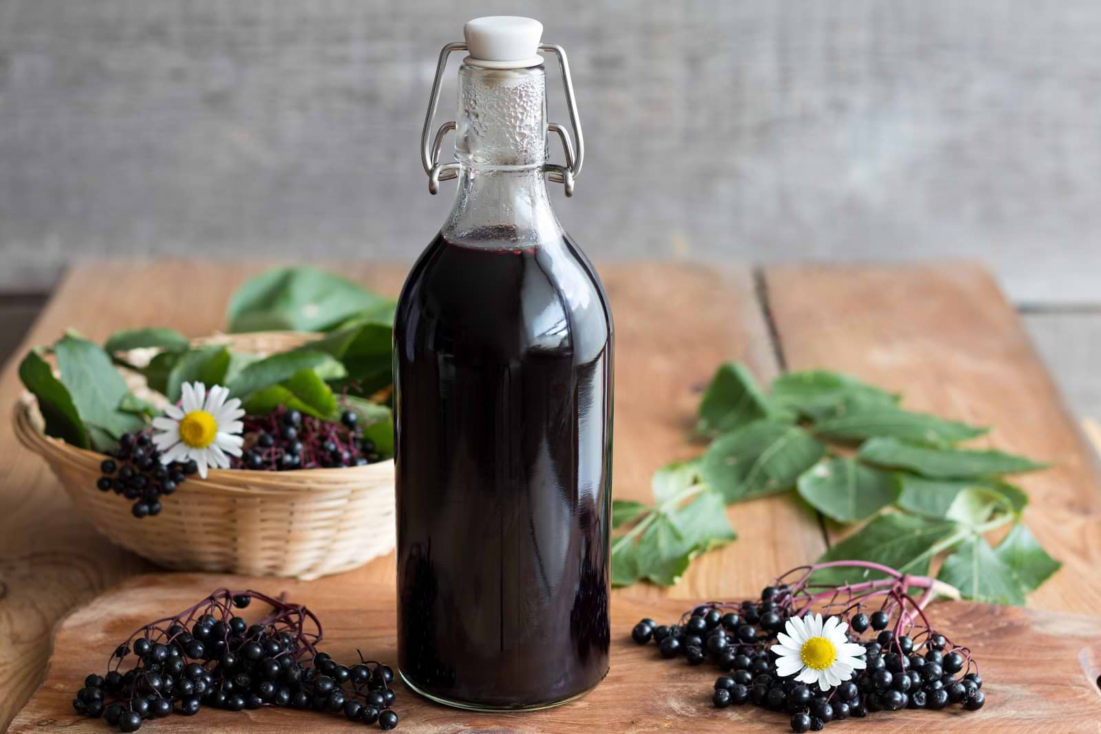 A bottle of elderberry juice next to piles of elderberries and antiviral herbs