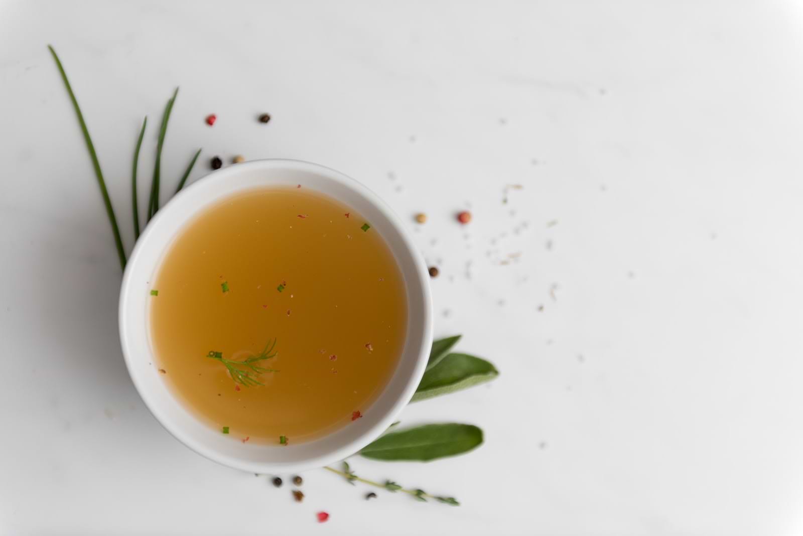 Where to buy bone broth: A cup of broth surrounded by leaves and peppercorns