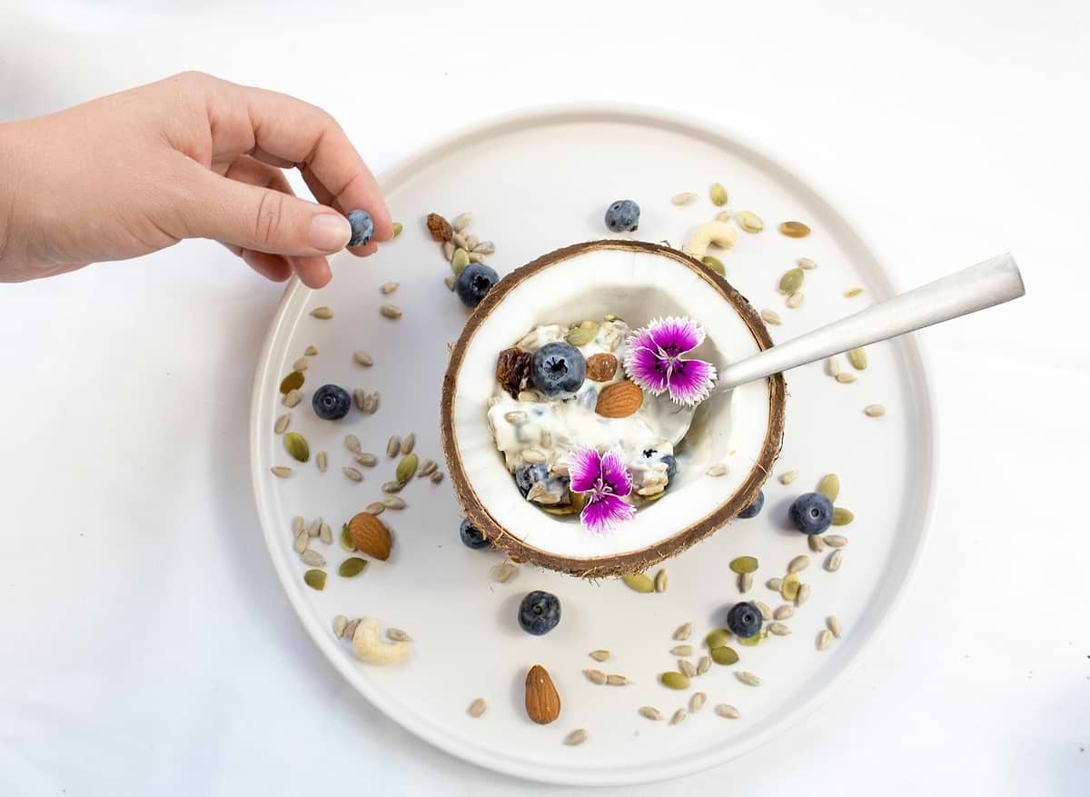 Kefir yogurt inside a coconut, surrounded by fruit, nuts, and flowers