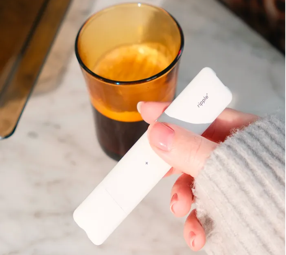 Close crop of a hand holding a ripple⁺ device next to a coffee