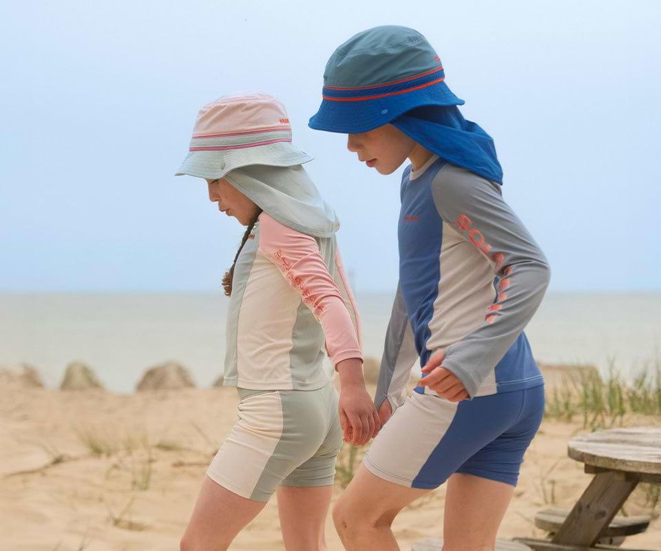Kids wearing UV Protective Clothing for Kids while walking on the beach in sun hats.