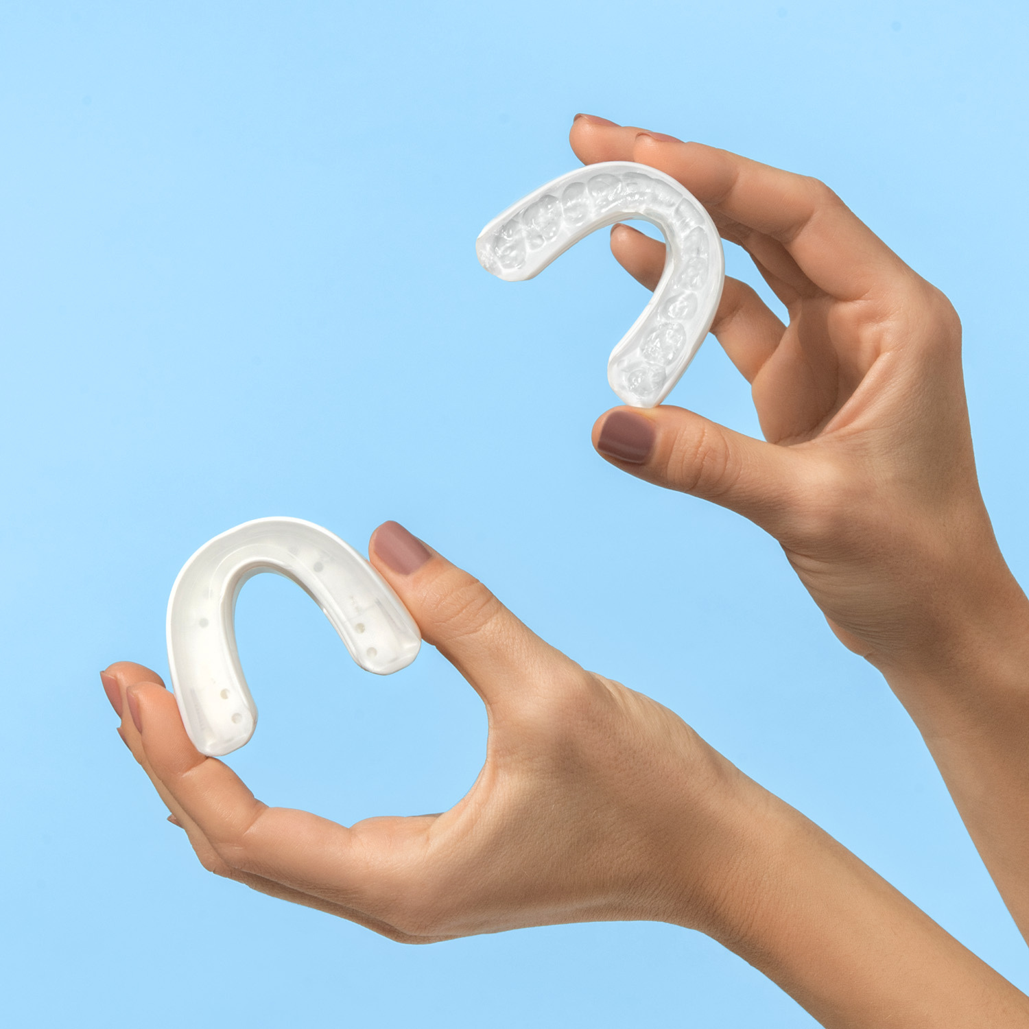 Two clear snore guards held by hands against a light blue background