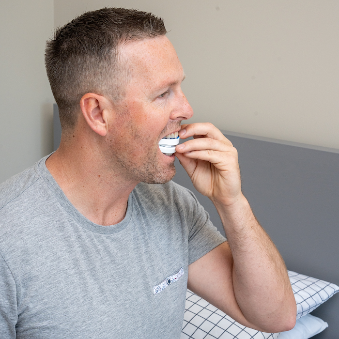 Man in a gray t-shirt using a mouthguard in a bedroom setting