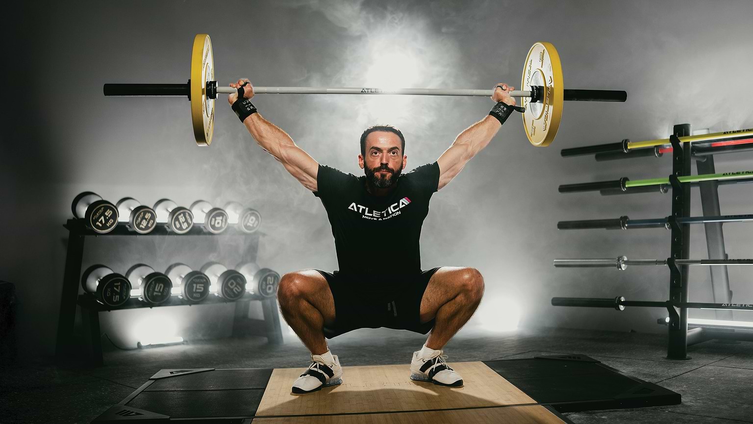 Athlet führt Overhead Squat mit Atletica Langhantel und Color Bumper Plates im Gym aus