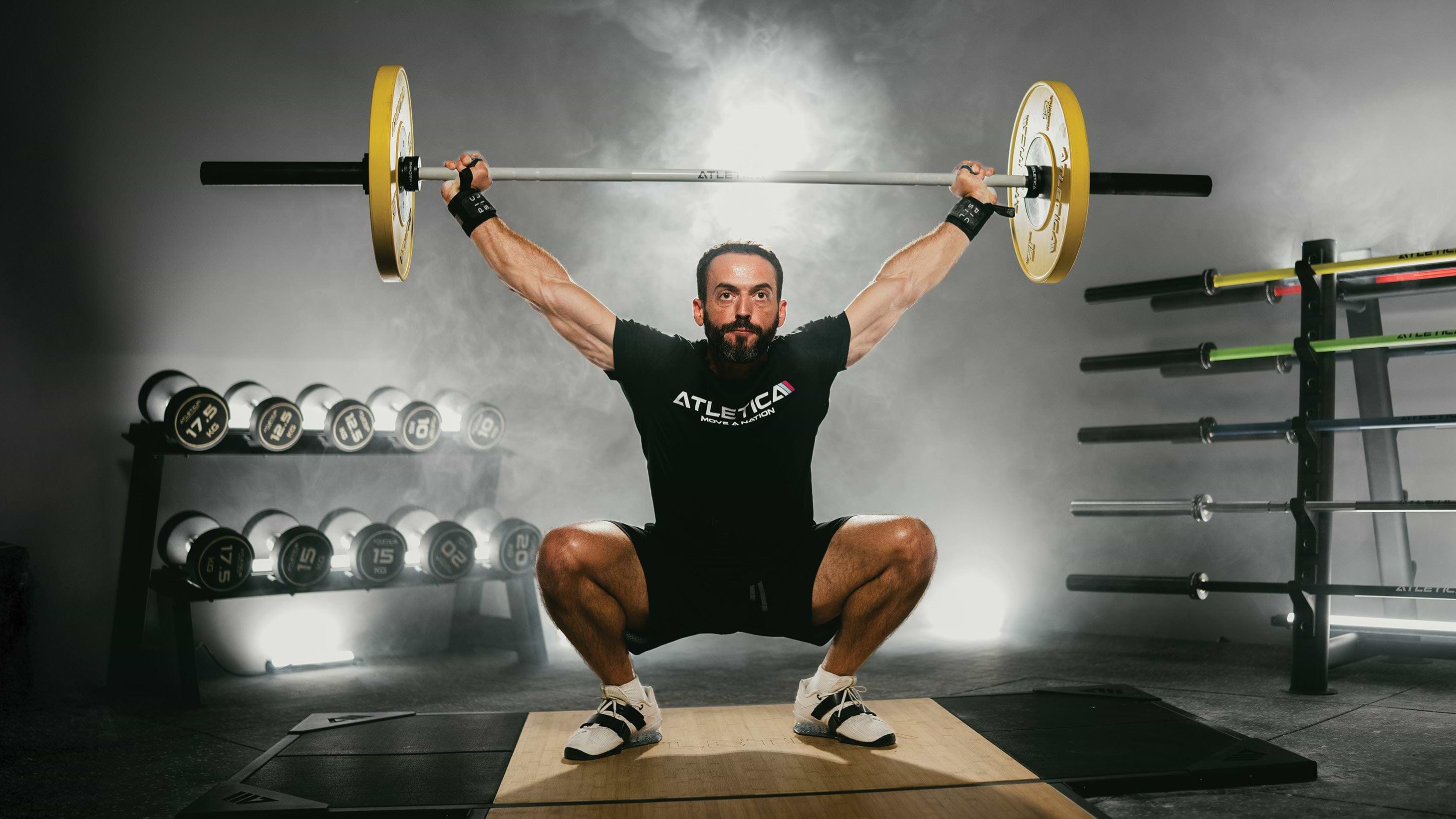 Athlet führt Overhead Squat mit Atletica Langhantel und Color Bumper Plates im Gym aus
