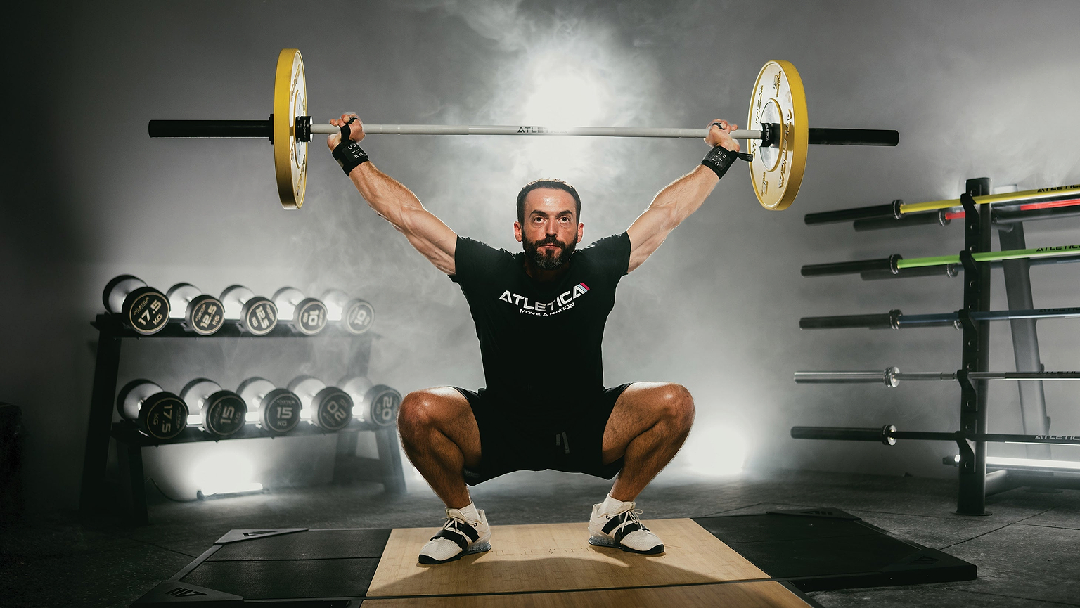 Athlet führt Overhead Squat mit Atletica Langhantel und Color Bumper Plates im Gym aus