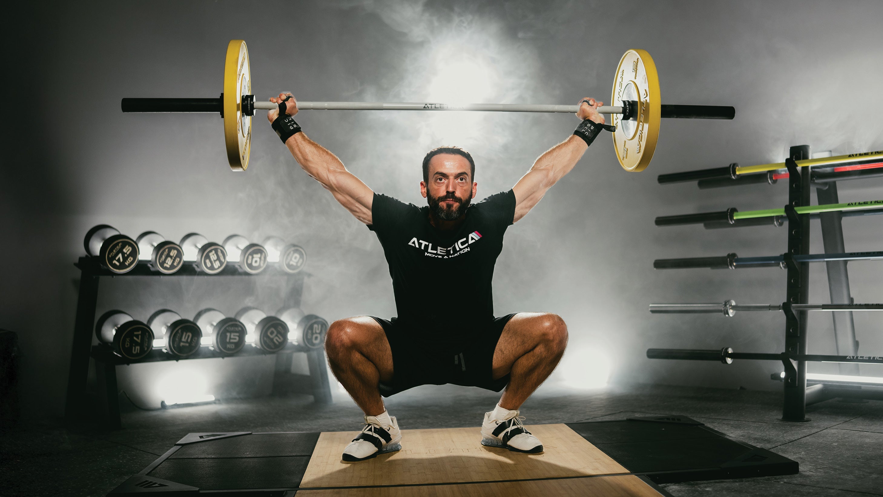 Athlet führt Overhead Squat mit Atletica Langhantel und Color Bumper Plates im Gym aus