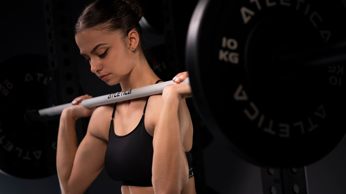Frau führt Back Squats mit weißer Atletica Langhantelstange und 10 kg Bumper Plates aus
