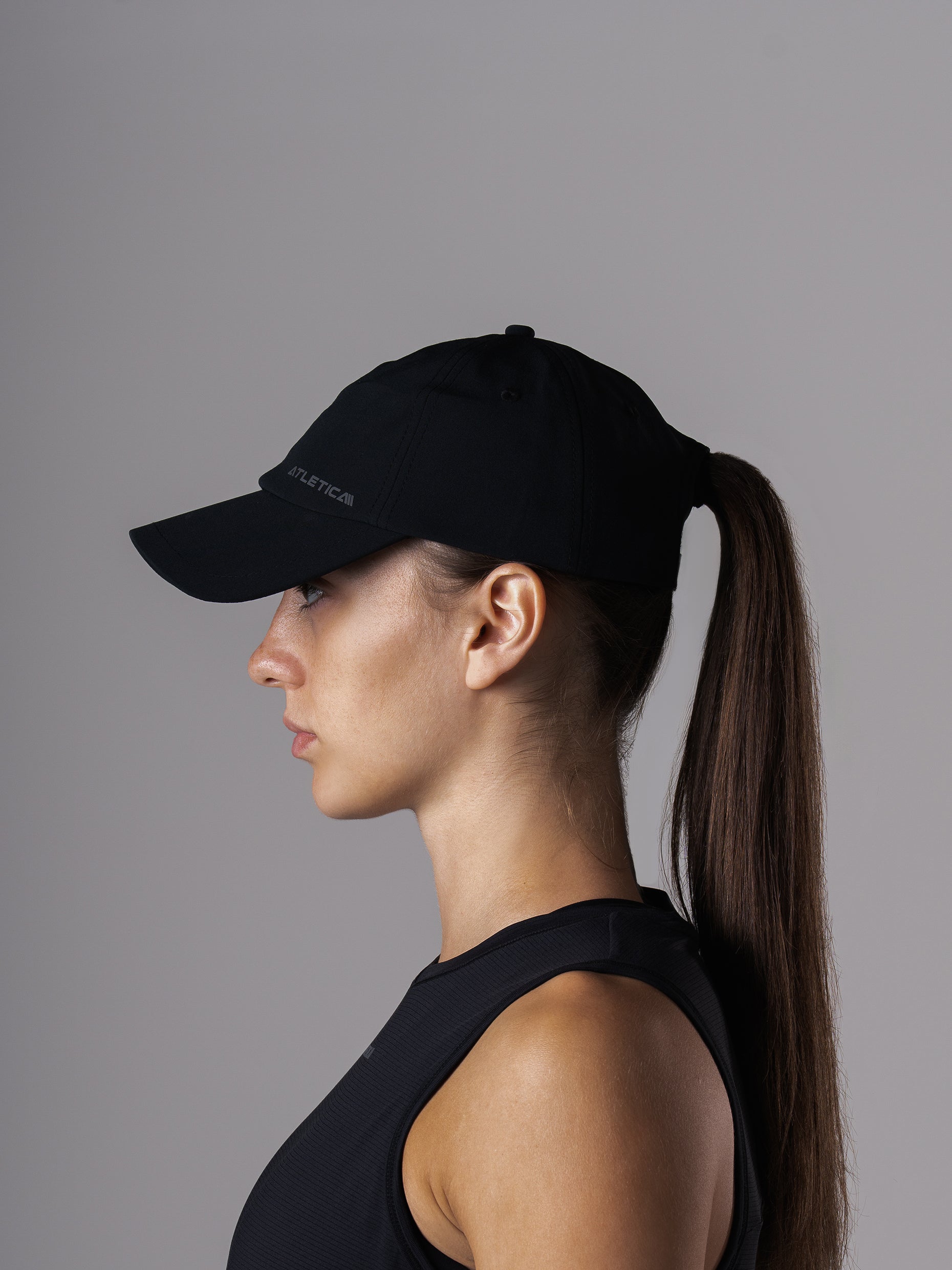 Seitenansicht der schwarzen Cool Cap von Atletica an einer Frau mit Pferdeschwanz