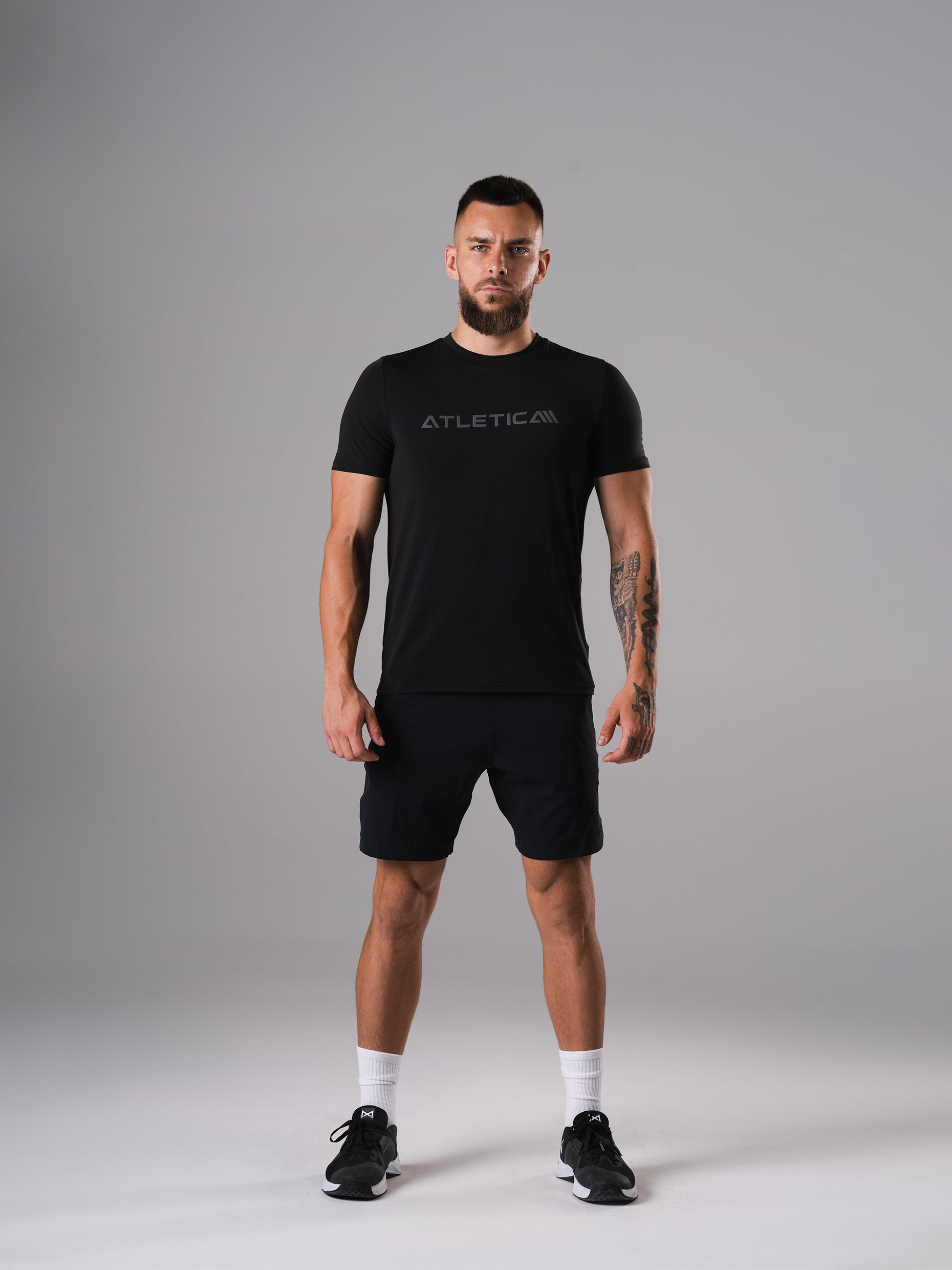Ganzkörperansicht: Mann im Merch Flex Train T-Shirt in Schwarz von Atletica mit schwarzen Shorts